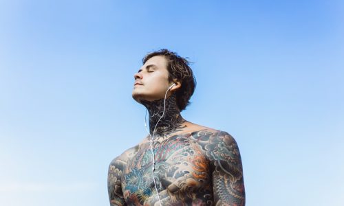 tattooed-man-with-headphones-against-blue-sky-ocean_1321-846