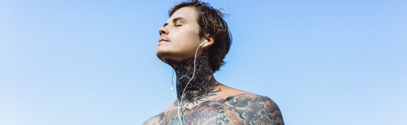 tattooed-man-with-headphones-against-blue-sky-ocean_1321-846
